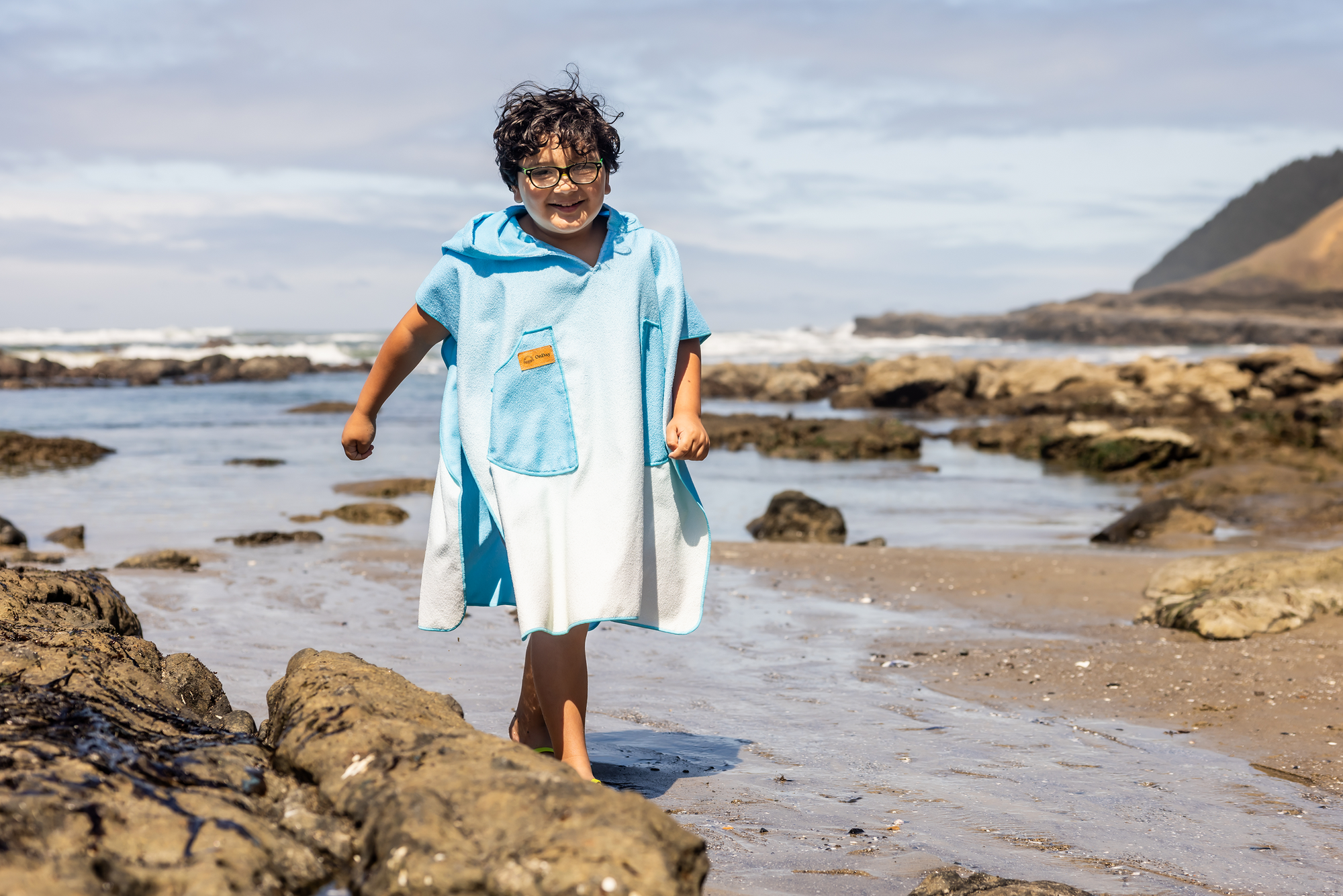 Person on a beach wearing a colorful poncho towel with ocean and rocks in the background