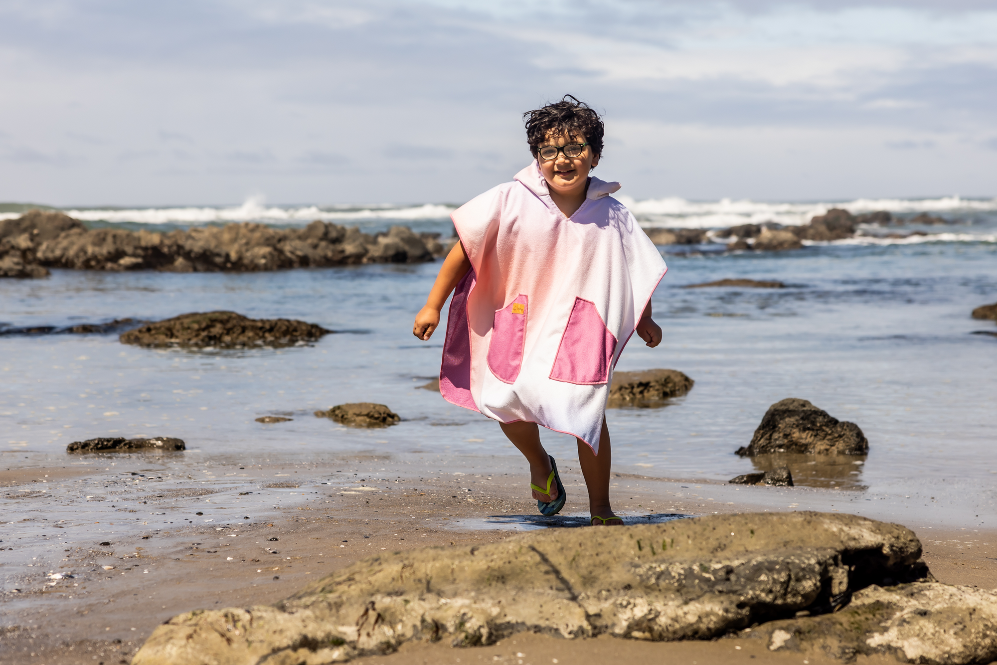 Person on a beach wearing a colorful poncho towel with ocean and rocks in the background
