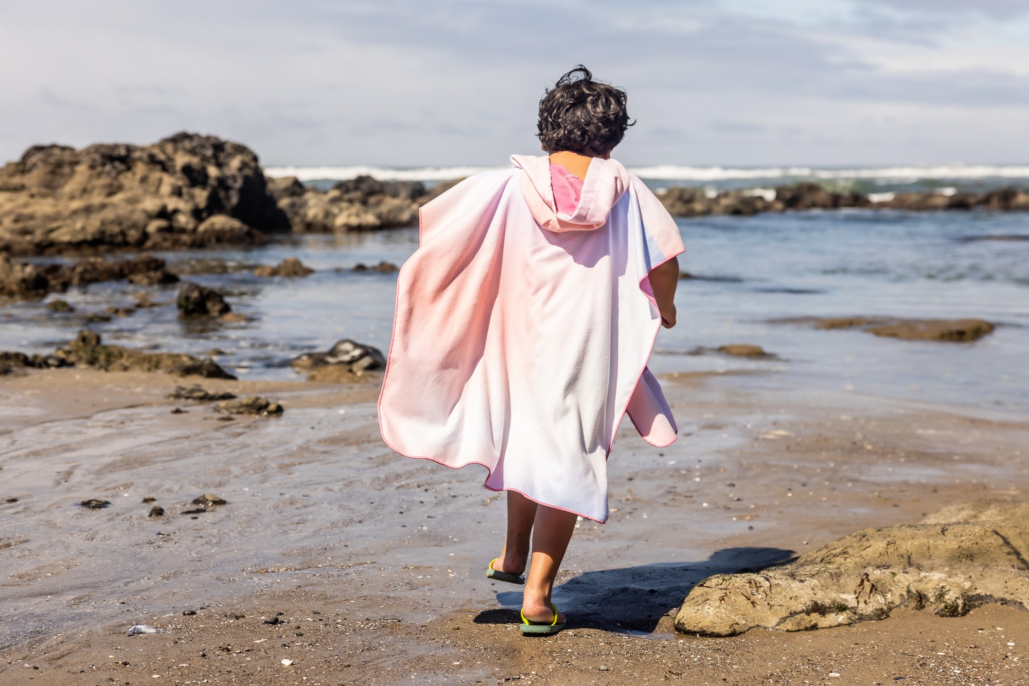 Person on a beach wearing a colorful poncho towel with ocean and rocks in the background