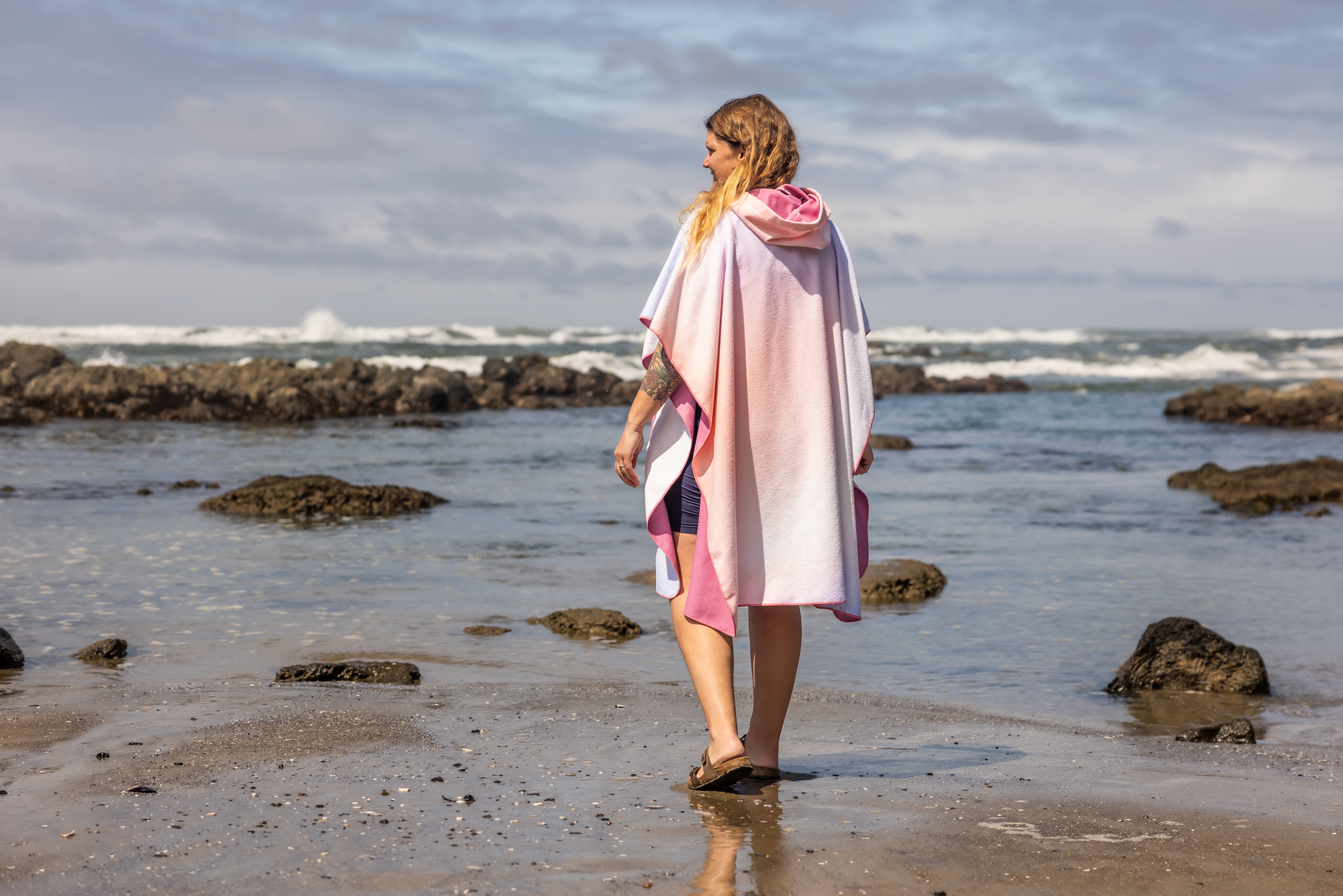 Person on a beach wearing a colorful poncho towel with ocean and rocks in the background