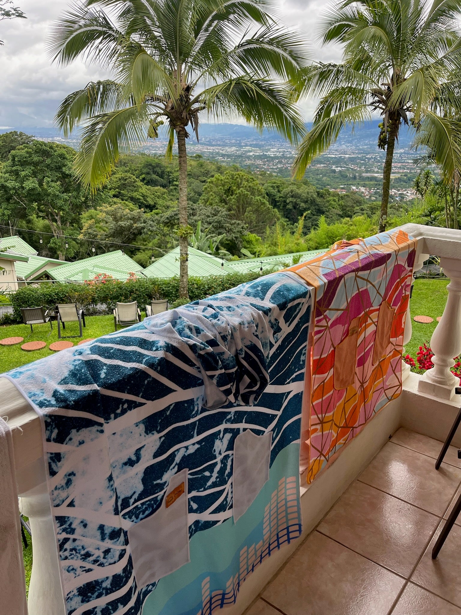 Colorful towels hanging on a railing with a scenic view of trees and mountains in the background.