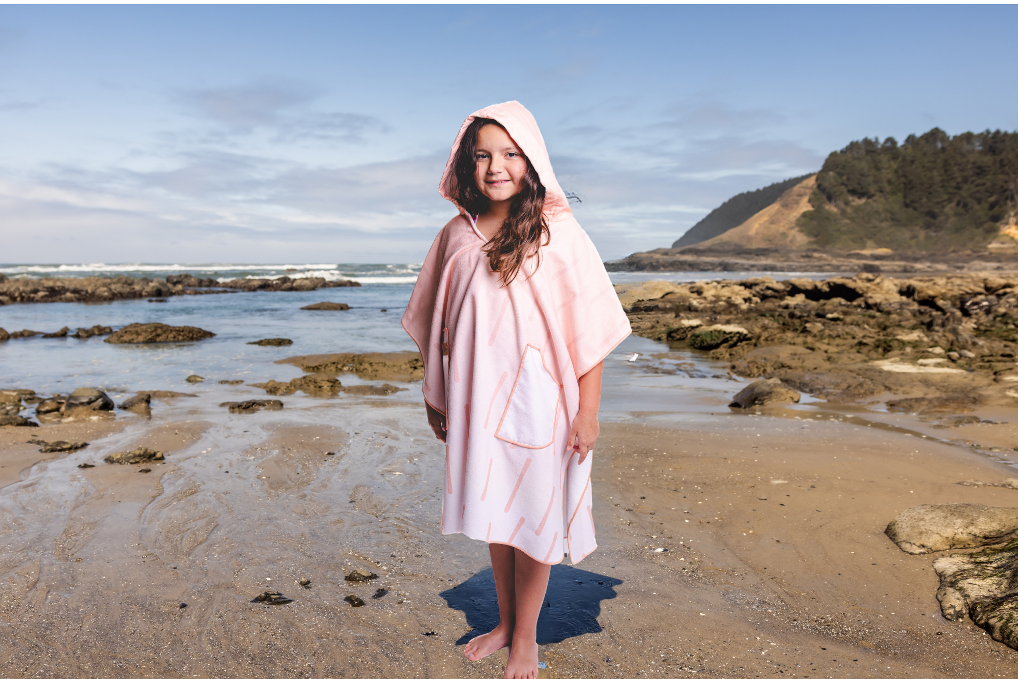 Person on a beach wearing a colorful poncho towel with ocean and rocks in the background