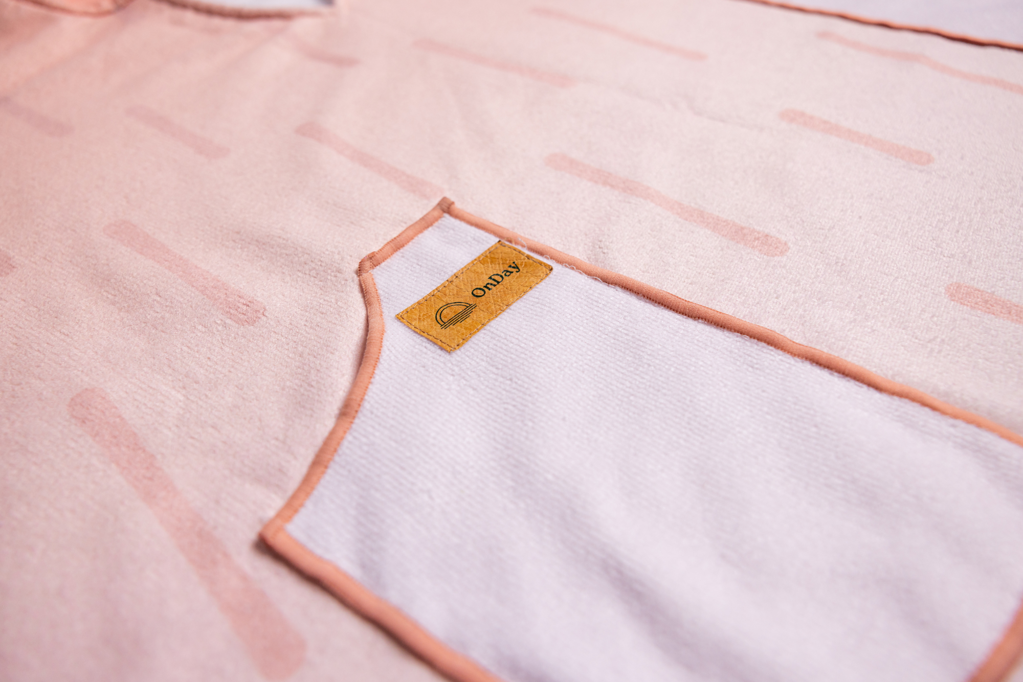 Fabric close up of towel poncho, pink with lines and pockets. 