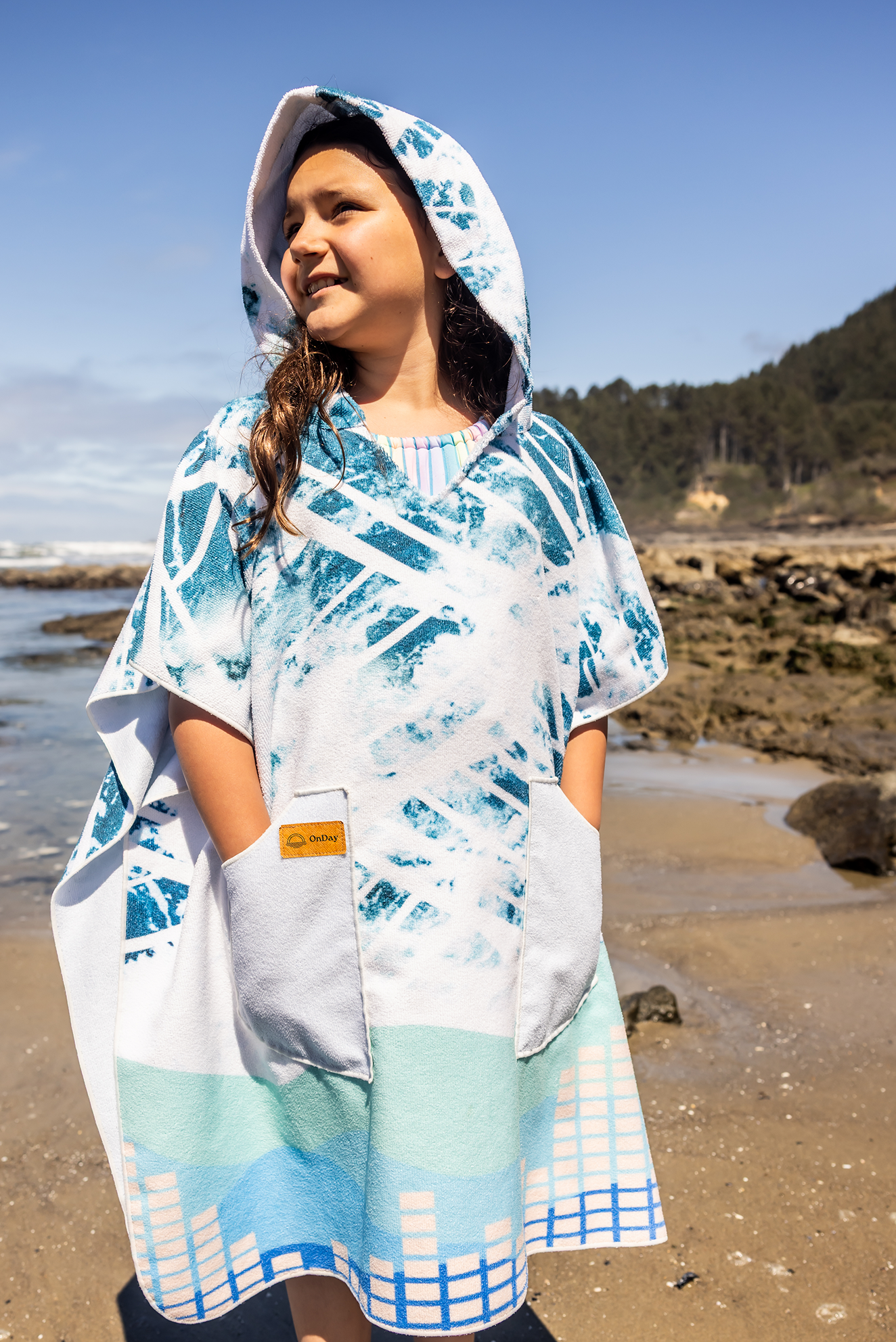 Person on a beach wearing a colorful poncho towel with ocean and rocks in the background