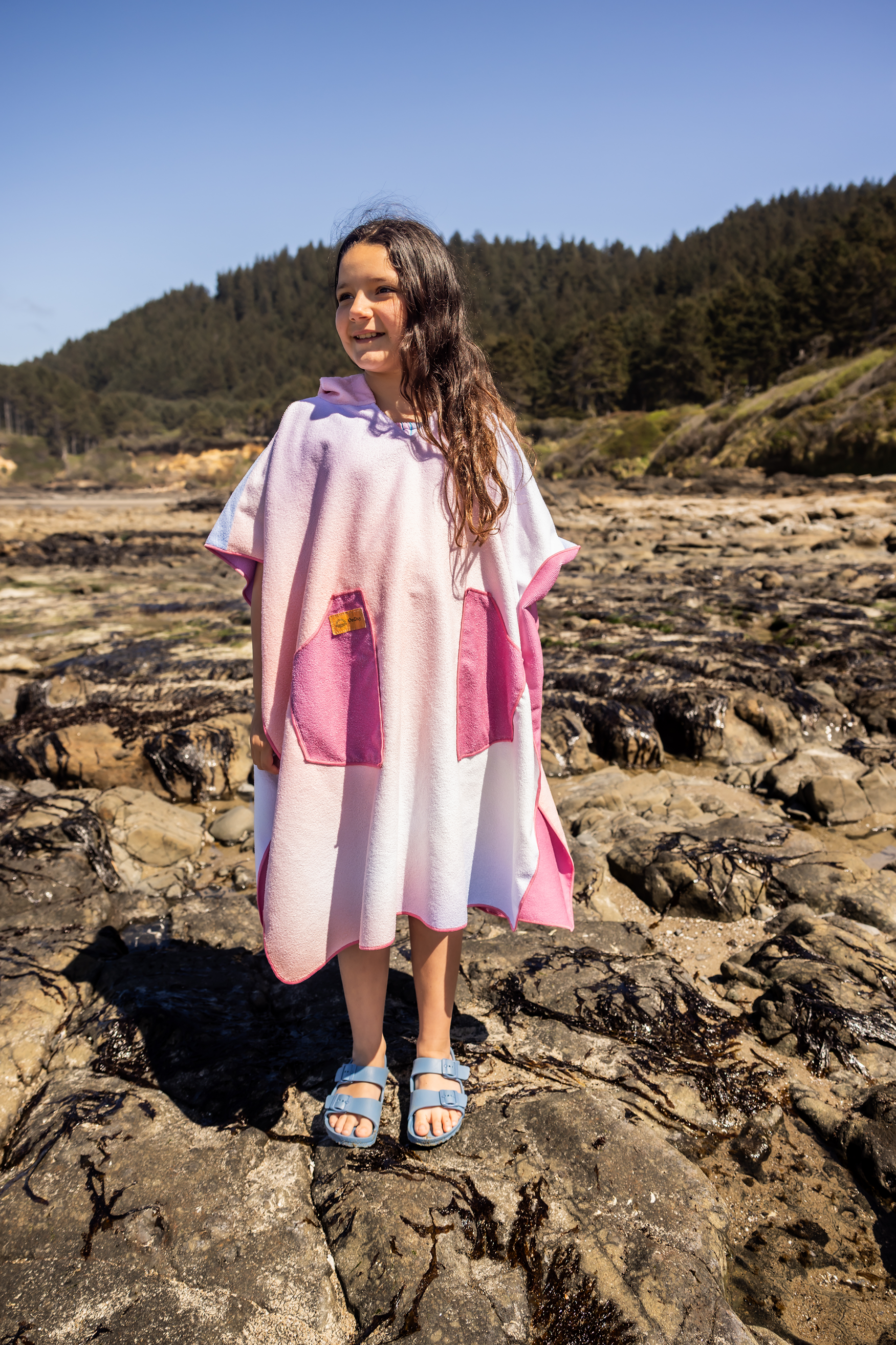 Person on a beach wearing a colorful poncho towel with ocean and rocks in the background