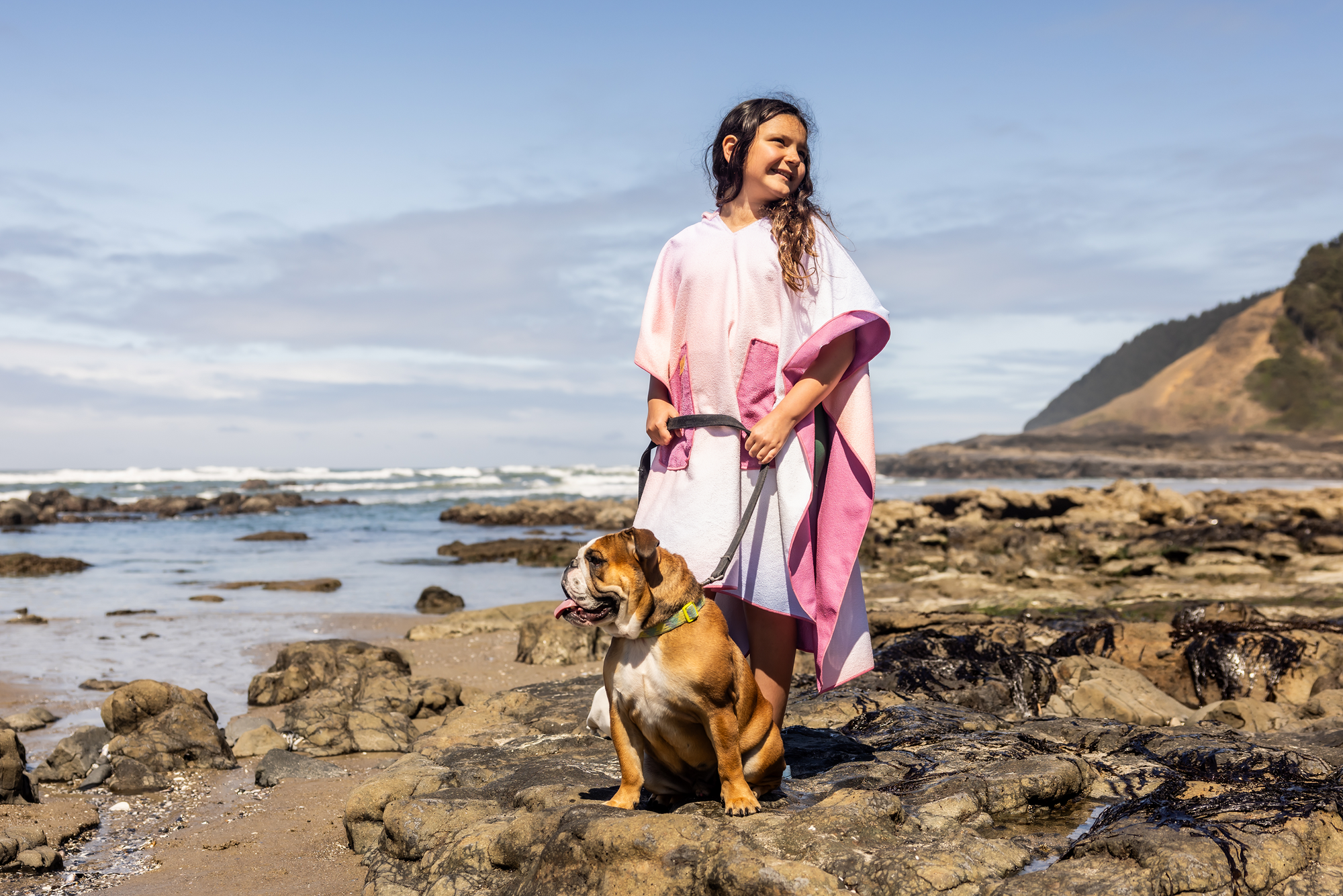 Person on a beach wearing a colorful poncho towel with ocean and rocks in the background