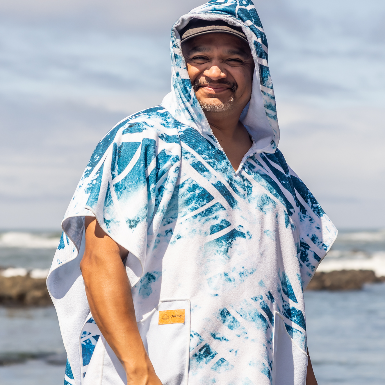 Person on a beach wearing a colorful poncho towel with ocean and rocks in the background