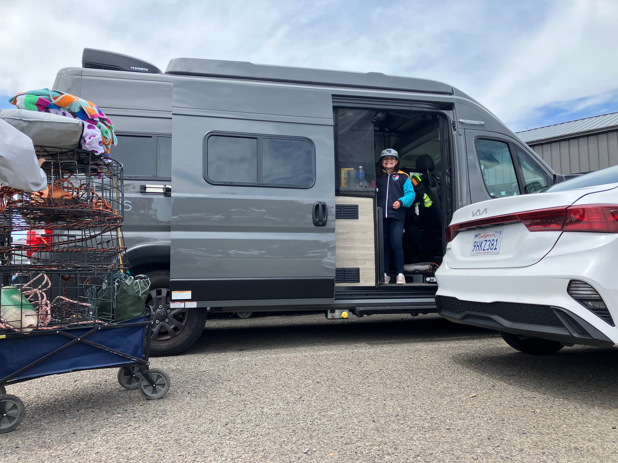 Person exiting a van with a cart full of items on a cloudy day.